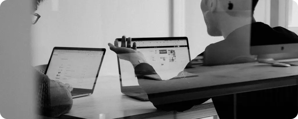 Zwart-wit foto van professionals die projecten bespreken in een moderne kantooromgeving, met de nadruk op teamwork, zakelijke communicatie en corporate samenwerking.