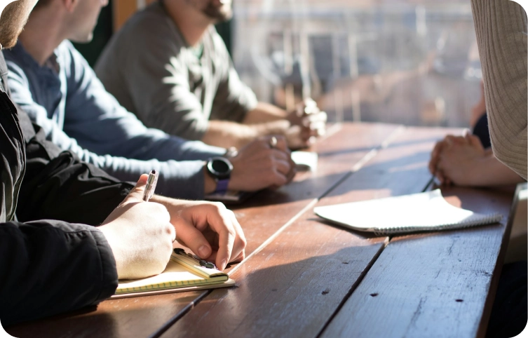 Groep professionals die deelnemen aan een samenwerkingsvergadering, ideeën uitwisselend en zakelijke strategieën besprekend rond een conferentietafel.